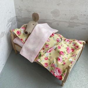Könnte beinhalten: Ein kleines Holzbett mit einem Bettwäsche-Set mit rosafarbenem und gelbem Blumenmuster. Eine Stoffmaus liegt im Bett.