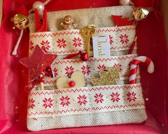 May include: A Christmas-themed burlap advent calendar with red and white snowflake pattern. The calendar has pockets holding miniature ornaments like a gingerbread man, a gold key, a candy cane, and a star. The calendar is inside a cardboard box.
