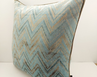 Könnte beinhalten: Ein blaues und braunes Kissen mit Chevron-Muster und braunem Stoffrand. Das Kissen hat ein "Secret"-Etikett unten rechts.