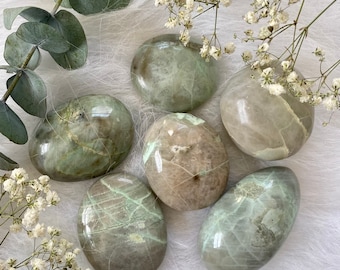 May include: Six smooth, polished green and white stones with a marbled pattern. The stones are arranged on a white fuzzy surface.