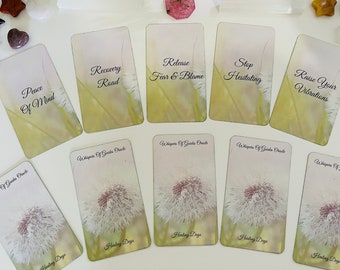 Puede incluir: Un conjunto de cartas de oráculo con afirmaciones como "Paz Mental" y "Eleva tus Vibraciones". Las cartas presentan un fondo floral y están acompañadas de cristales y piedras preciosas.