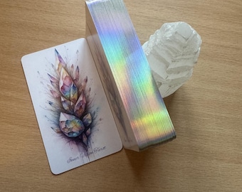 May include: A deck of tarot cards with a holographic iridescent back. The card on top features a watercolor illustration of a crystal cluster with the text "Inner Vision Force".
