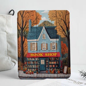 May include: A blue and white building with a red awning that says "Book Shop". The building is surrounded by trees with orange and yellow leaves. The building has a window display with books and plants.