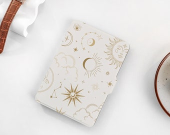 May include: A white e-reader cover with a gold celestial pattern. The pattern includes moons, stars, clouds, and a sun with a face.