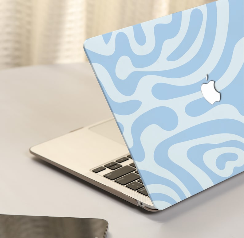 K&ouml;nnte beinhalten: Ein hellblauer Laptop mit einem wei&szlig;en und hellblauen abstrakten Muster auf dem Deckel. Der Laptop ist ge&ouml;ffnet und die Tastatur ist sichtbar. Das Apple-Logo befindet sich auf dem Deckel.