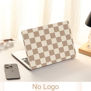 May include: A laptop computer with a brown and white checkered design on the lid. The laptop is on a white surface with a cell phone and a watch.