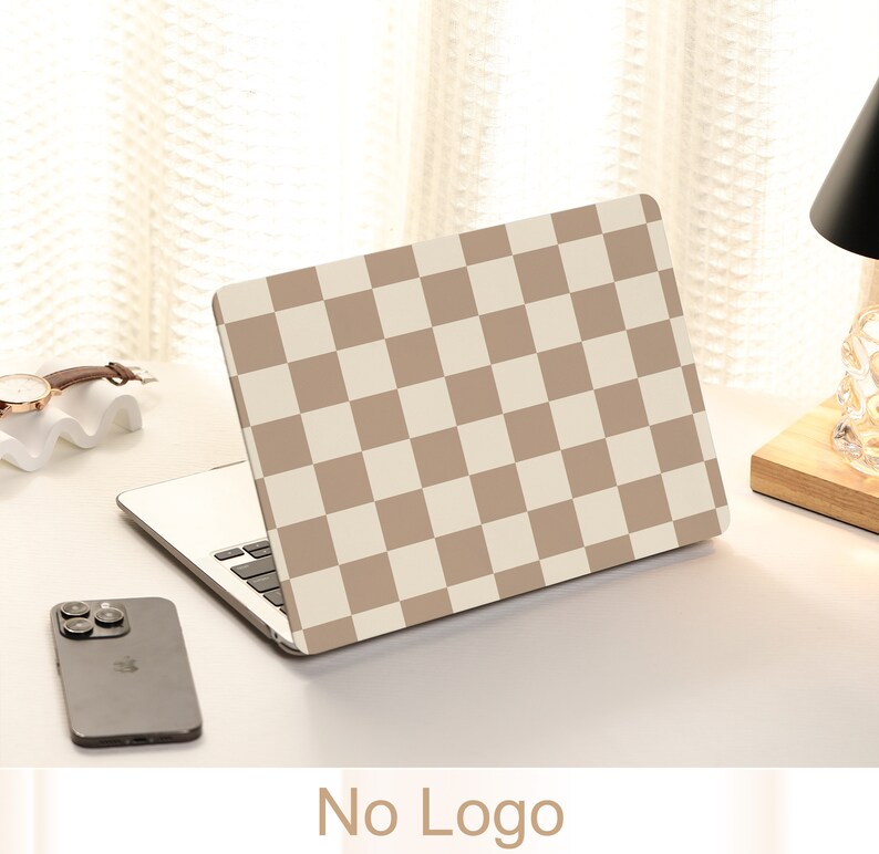 May include: A laptop computer with a brown and white checkered design on the lid. The laptop is on a white surface with a cell phone and a watch.