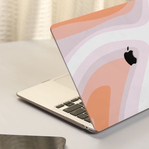 May include: A laptop computer with a pink, orange, and white abstract swirl design on the lid. The laptop is closed and sitting on a white surface.