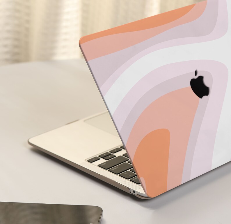 May include: A laptop computer with a pink, orange, and white abstract swirl design on the lid. The laptop is closed and sitting on a white surface.