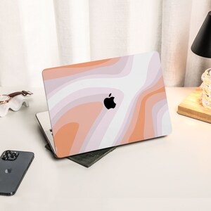 May include: A closed laptop computer with a white and orange abstract design on the lid. The Apple logo is visible on the lid.