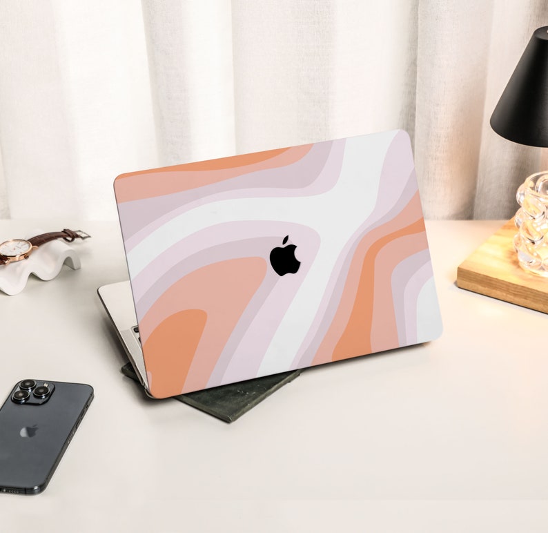 May include: A closed laptop computer with a white and orange abstract design on the lid. The Apple logo is visible on the lid.