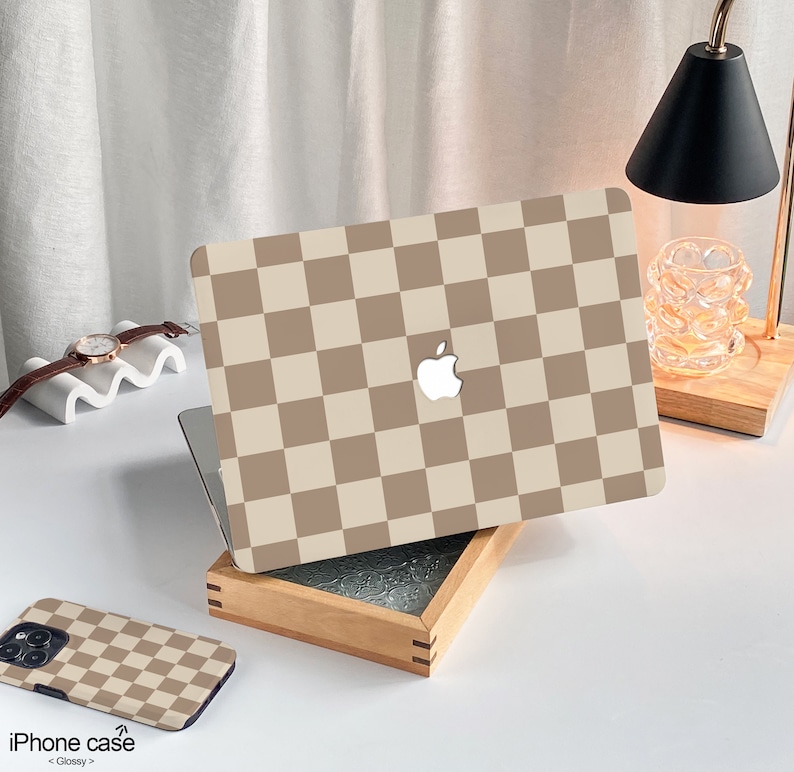May include: A brown and white checkered laptop skin with an Apple logo. The skin is on a wooden box with a glass top. The text "iPhone case < Glossy >" is on the bottom of the image.