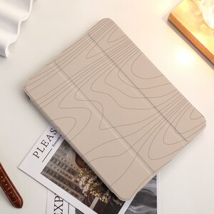May include: A beige iPad case with a wood grain pattern. The case has a fold-over flap and a magnetic closure.