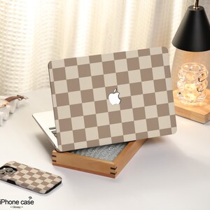 May include: A laptop computer with a brown and white checkered pattern on the lid. The laptop is closed and sitting on a wooden box. There is a brown and white checkered phone case next to the laptop.