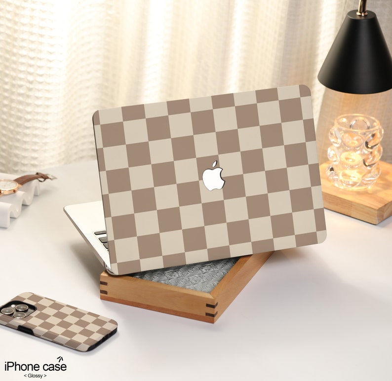 May include: A laptop computer with a brown and white checkered pattern on the lid. The laptop is closed and sitting on a wooden box. There is a brown and white checkered phone case next to the laptop.