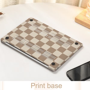 May include: A brown and beige checkered laptop case with a silver trim and rubber feet. The case is designed to protect a laptop from scratches and bumps.