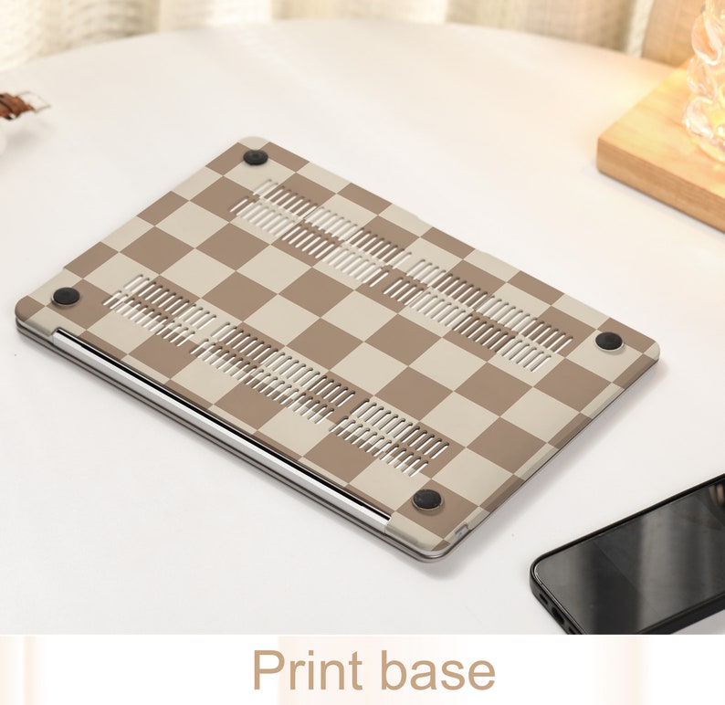 May include: A brown and beige checkered laptop case with a silver trim and rubber feet. The case is designed to protect a laptop from scratches and bumps.