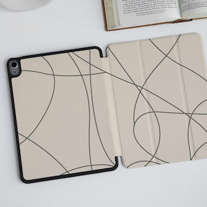 May include: A beige iPad case with a black border and a simple abstract design of black lines.