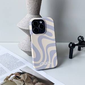 Op de afbeelding: Een lichtblauwe en cr&egrave;me telefoonhoes met een golvend abstract ontwerp. De hoes heeft een uitsparing voor de cameralens en een aangepaste inscriptie.