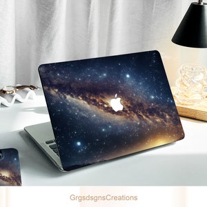 May include: A laptop computer with a galaxy-themed design. The laptop has a dark blue background with a swirling galaxy of stars and a white Apple logo.
