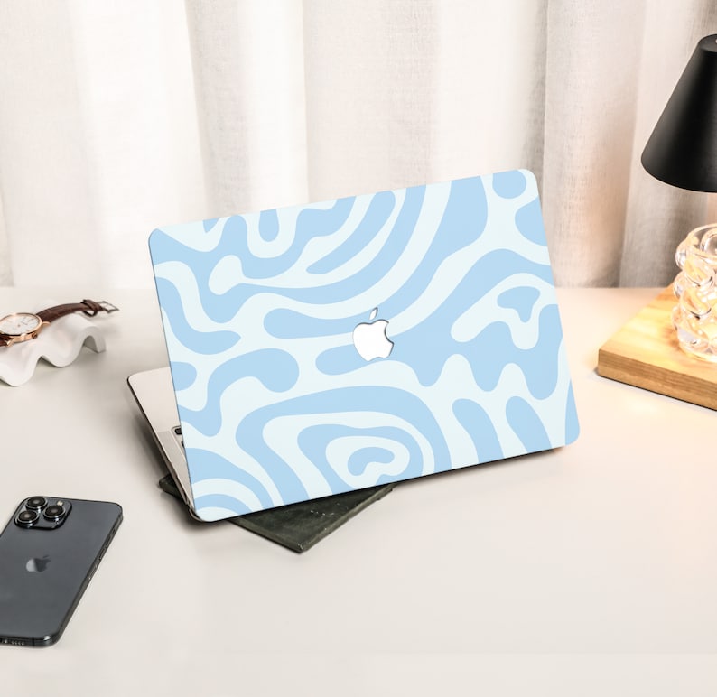 K&ouml;nnte beinhalten: Eine hellblaue Laptop-Haut mit einem wei&szlig;en abstrakten Wirbelmuster. Das Apple-Logo ist auf dem Laptop sichtbar.