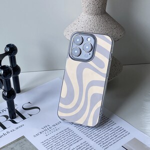 Op de afbeelding: Een transparante telefoonhoes met een abstract swirl-patroon in wit en grijs. De hoes is ontworpen voor een iPhone met een drievoudig camerasysteem.