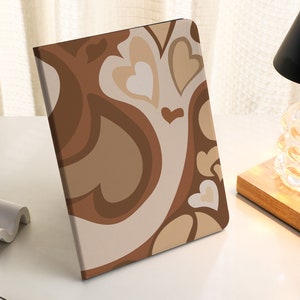 Op de afbeelding: Een bruine en beige notitieboekomslag met een draaiend patroon van harten. De omslag heeft een modern, abstract ontwerp.