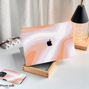 May include: A pink and white abstract swirl pattern laptop skin with an Apple logo. The skin is on a wooden box with a white surface underneath.