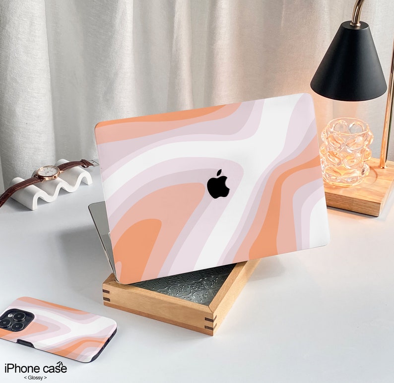 May include: A pink and white abstract swirl pattern laptop skin with an Apple logo. The skin is on a wooden box with a white surface underneath.