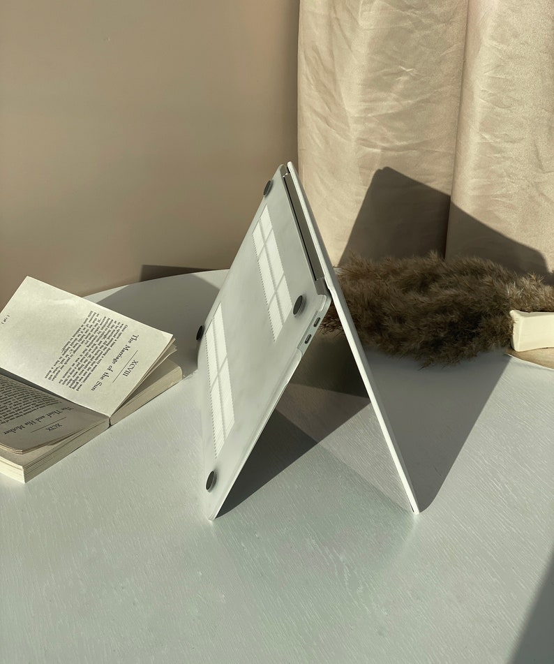 Op de afbeelding: Een witte laptophoes met een textuur en zwarte rubberen voetjes. De hoes is open en in een hoek gekanteld.