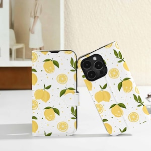May include: White phone case with a lemon pattern. The case features whole and sliced yellow lemons with green leaves scattered across the surface. The case is open, revealing the phone's camera.