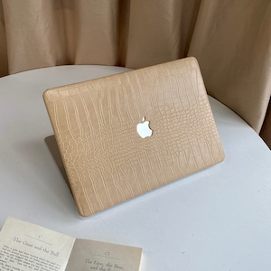 May include: A beige laptop case with a crocodile-embossed texture. The case has a silver Apple logo in the centre.