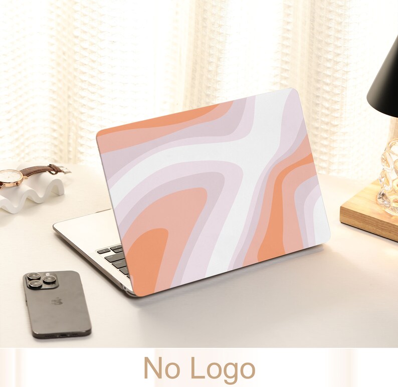 May include: A laptop computer with a pink and orange abstract design on the lid. The laptop is closed and sitting on a white surface.