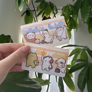 May include: A white ceramic mug with a black handle and the text "But First, Coffee" in a bold, black font. The mug is set against a blurred background, suggesting a cozy setting.