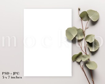 Puede incluir: Una maqueta de tarjeta blanca en blanco con una rama de hojas de eucalipto sobre un fondo gris claro. La tarjeta mide 5 x 7 pulgadas.