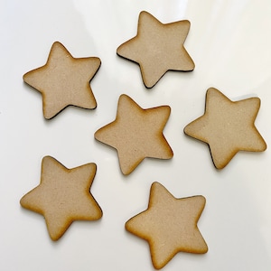 May include: Six unfinished wooden star cutouts. Each star has five points and a light brown color. The stars are arranged on a white surface. These stars are suitable for crafting and DIY projects.