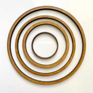 May include: Four wooden embroidery hoops of different sizes, nested inside each other. The hoops are all brown and have a natural wood finish.