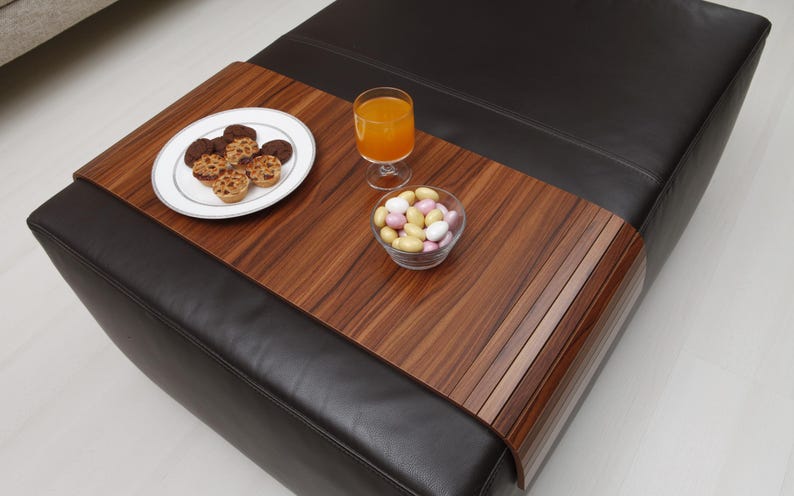K&ouml;nnte beinhalten: Ein Tablett aus Holz mit einer schwarzen Lederbasis. Das Tablett besteht aus d&uuml;nnen Holzlatten und hat eine nat&uuml;rliche Holzoptik. Das Tablett liegt auf einem schwarzen Ledersessel. Auf dem Tablett befinden sich Snacks und ein Glas Orangensaft.