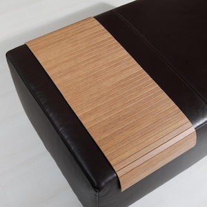 Può includere: Un pouf in pelle nera con un vassoio estraibile in legno. Il vassoio è in legno marrone chiaro con un design a doghe.