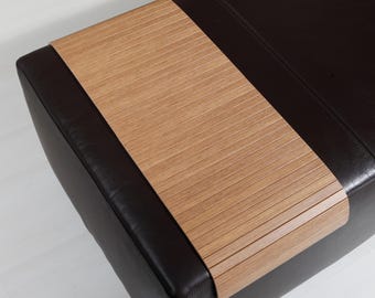 Könnte beinhalten: Ein schwarzer Lederhocker mit einem ausziehbaren Holztablett. Das Tablett ist aus hellem braunem Holz mit einem Lamellendesign.