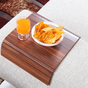 K&ouml;nnte beinhalten: Ein Holztablett mit abgerundeter Kante steht auf einem wei&szlig;en Sofa. Auf dem Tablett befinden sich ein Glas Orangensaft und eine wei&szlig;e Sch&uuml;ssel gef&uuml;llt mit Tortilla-Chips.