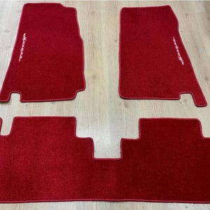 Puede incluir: Un juego de cuatro alfombrillas rojas para coche. Las alfombrillas están hechas de un material afelpado y tienen una inscripción blanca bordada. Las alfombrillas están diseñadas para adaptarse a los huecos de los pies delanteros y traseros de un vehículo.
