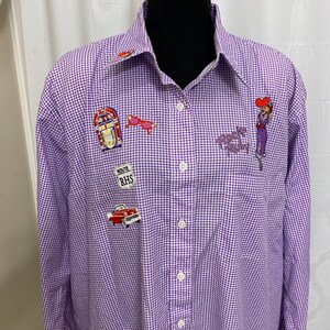 May include: A purple and white gingham button-down shirt with embroidered patches of a jukebox, sunglasses, a car, and a woman. The shirt has a pointed collar and long sleeves. The text "Rock's Friday" is embroidered on the chest.