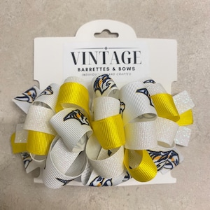 May include: A handmade hair bow with white, yellow, and glittery white ribbons. The bow features a repeating pattern of a stylized bird logo. The packaging reads "VINTAGE BARRETTES & BOWS INDIVIDUALLY HAND CRAFTED."