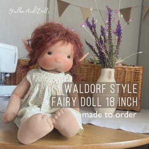 Może przedstawiać: Lalka wróżka w stylu Waldorf, o wysokości około 46 cm, z rudymi włosami i spiczastymi uszami. Lalka ma na sobie sukienkę w kwiaty i miękki, materiałowy korpus. Tekst na zdjęciu brzmi "Waldorf Style Fairy Doll 18 inch made to order."