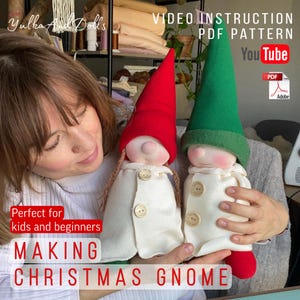 May include: Two handmade Christmas gnomes with red and green pointed hats, white coats, and button details. The image includes text that says "Video Instruction PDF Pattern" and "Making Christmas Gnome". The gnomes are held by a person.