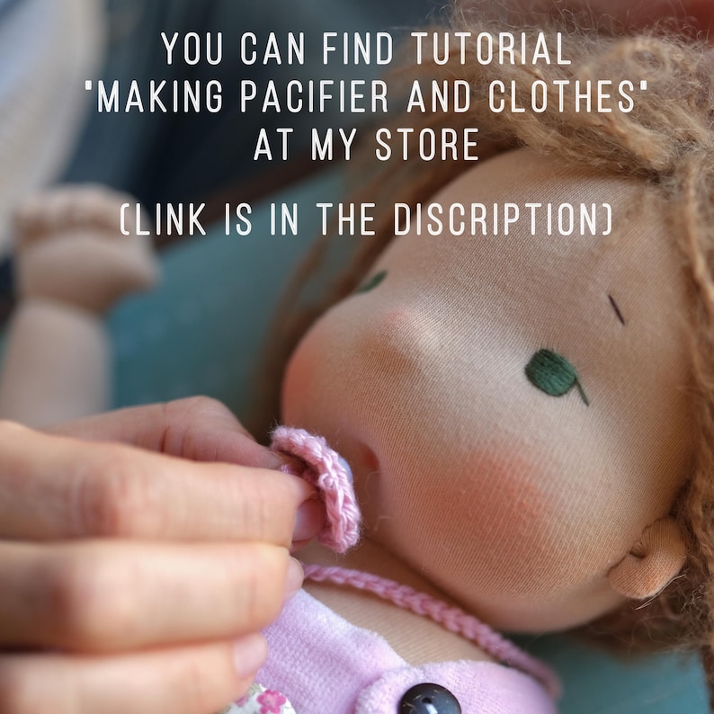 May include: A handmade doll with light brown hair and green embroidered eyes. The doll is wearing a pink outfit and a pink pacifier is being placed in its mouth. Text on the image reads: "YOU CAN FIND TUTORIAL 'MAKING PACIFIER AND CLOTHES' AT MY STORE (LINK IS IN THE DISCRIPTION)"