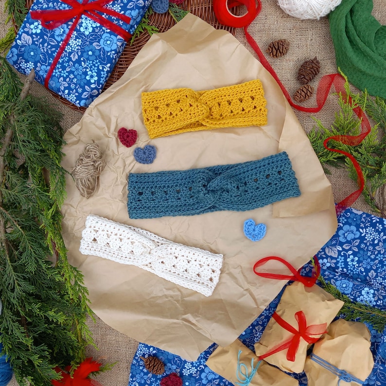 May include: Three handmade crochet headbands in yellow, teal, and white, displayed on brown paper with decorative elements. The headbands have a twisted design. The scene includes small heart-shaped embellishments and wrapped gifts with red ribbons.