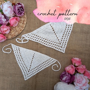 May include: Two white crochet triangle scarves with a lacy design are displayed on a brown surface. The words "crochet pattern PDF" are written in cursive. Pink and purple flowers and a ball of white yarn are also in the image.