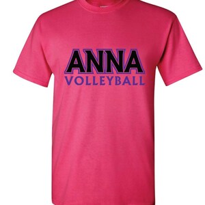 K&ouml;nnte beinhalten: Pinkes T-Shirt mit schwarzem Text, der "ANNA VOLLEYBALL" in einer fetten, umrandeten Schrift mit violetten Akzenten sagt.